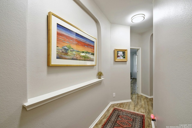 corridor with arched walkways, wood finished floors, and baseboards