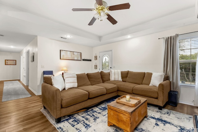 living area with ceiling fan, wood finished floors, visible vents, baseboards, and a raised ceiling