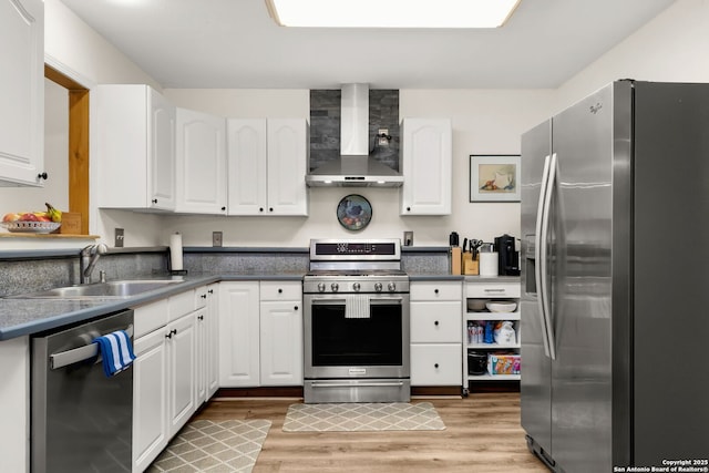 kitchen with stainless steel appliances, light wood-style floors, white cabinets, a sink, and wall chimney exhaust hood