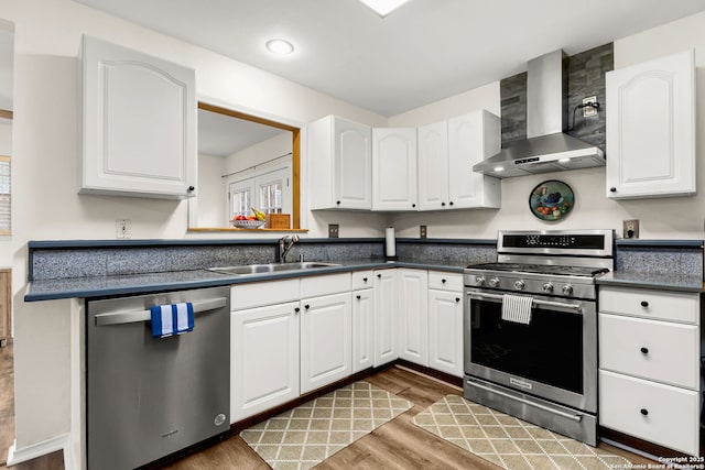 kitchen with appliances with stainless steel finishes, white cabinets, a sink, and wall chimney exhaust hood