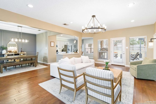 living area with recessed lighting, wood-type flooring, an inviting chandelier, a textured ceiling, and baseboards