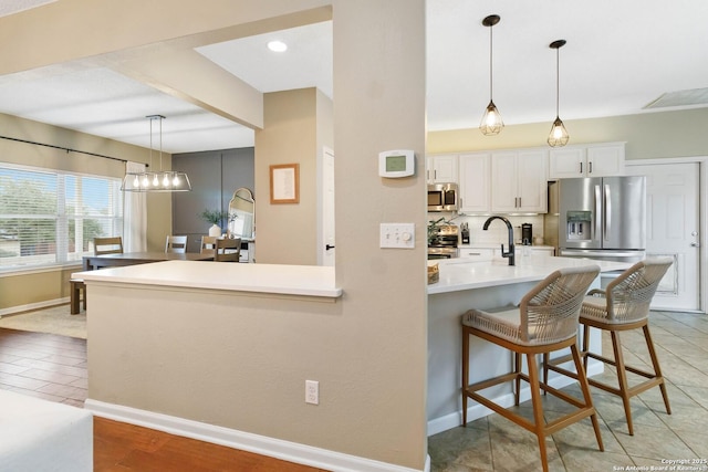 kitchen featuring stainless steel appliances, a breakfast bar, white cabinetry, light countertops, and hanging light fixtures