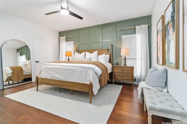 bedroom with dark wood-style floors, arched walkways, a decorative wall, and a ceiling fan