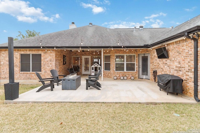 rear view of house with brick siding, roof with shingles, a chimney, an outdoor fire pit, and a patio area