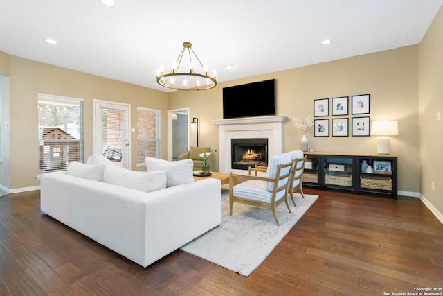 living room featuring a notable chandelier, dark wood finished floors, recessed lighting, a lit fireplace, and baseboards