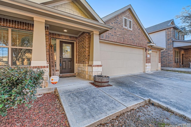 doorway to property with brick siding, a porch, a garage, stone siding, and driveway