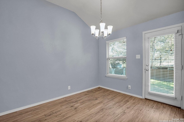 spare room with light wood-type flooring, vaulted ceiling, a notable chandelier, and baseboards