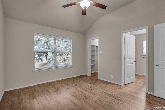 unfurnished bedroom featuring light wood finished floors, a spacious closet, baseboards, and vaulted ceiling