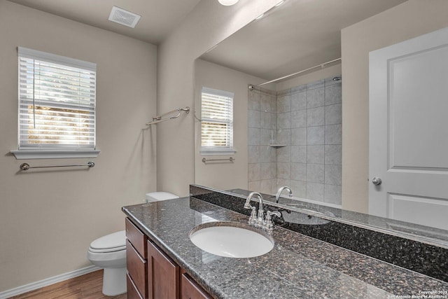 bathroom with toilet, wood finished floors, vanity, visible vents, and a shower