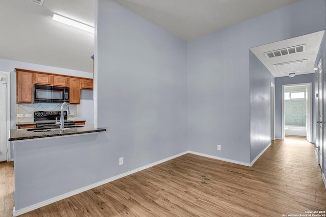 kitchen featuring black microwave, a peninsula, a sink, visible vents, and brown cabinetry