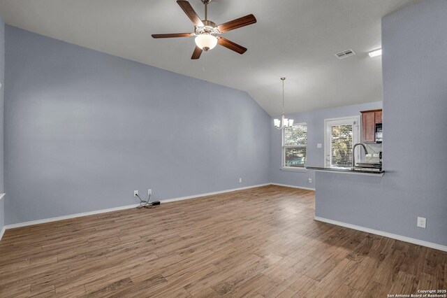 interior space with baseboards, visible vents, wood finished floors, vaulted ceiling, and ceiling fan with notable chandelier