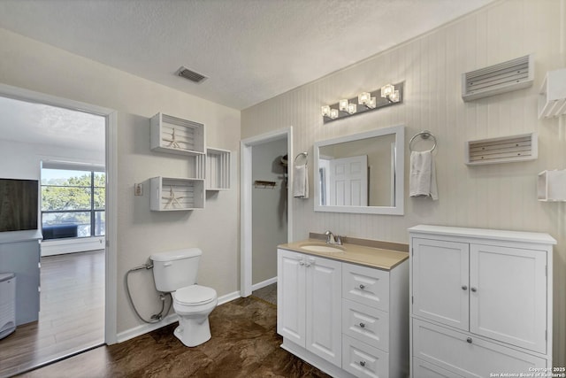 bathroom featuring visible vents, baseboards, toilet, vanity, and a textured ceiling