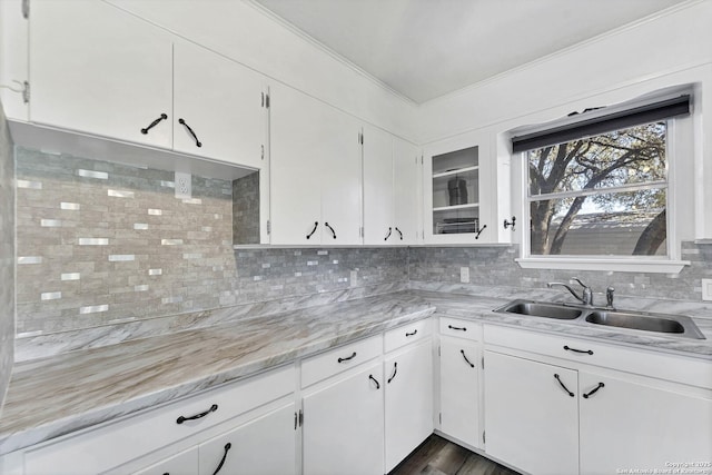 kitchen with white cabinetry, ornamental molding, backsplash, and a sink