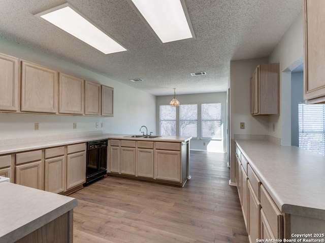 kitchen with black dishwasher, a peninsula, hanging light fixtures, light countertops, and a sink