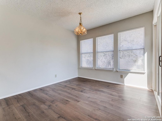 empty room featuring a wealth of natural light, a notable chandelier, a textured ceiling, and wood finished floors