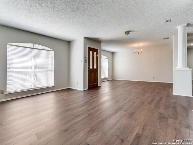 unfurnished living room featuring visible vents, dark wood finished floors, decorative columns, and a notable chandelier