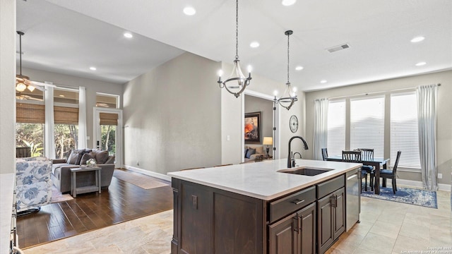 kitchen with dishwasher, open floor plan, a kitchen island with sink, light countertops, and a sink