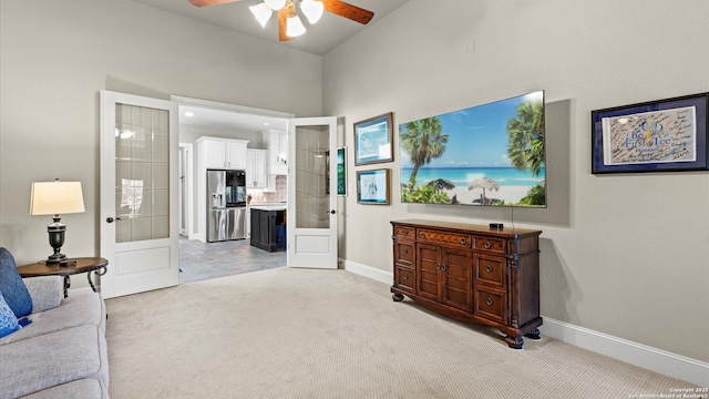 living area featuring a ceiling fan, french doors, light carpet, and baseboards