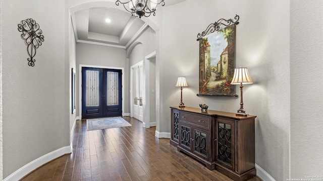 foyer with an inviting chandelier, a raised ceiling, baseboards, and wood finished floors