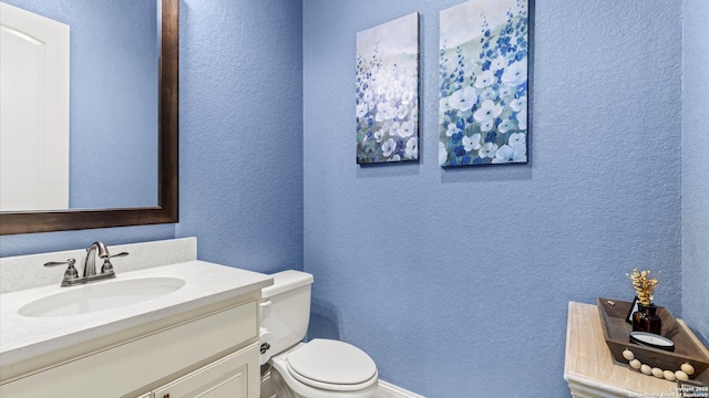 bathroom with a textured wall, vanity, and toilet