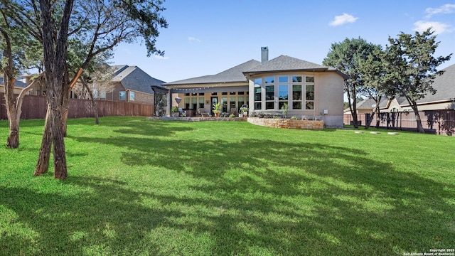 rear view of property featuring a yard, a chimney, a patio area, and a fenced backyard