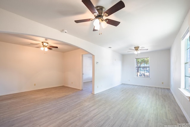 spare room featuring light wood-style floors, arched walkways, and baseboards