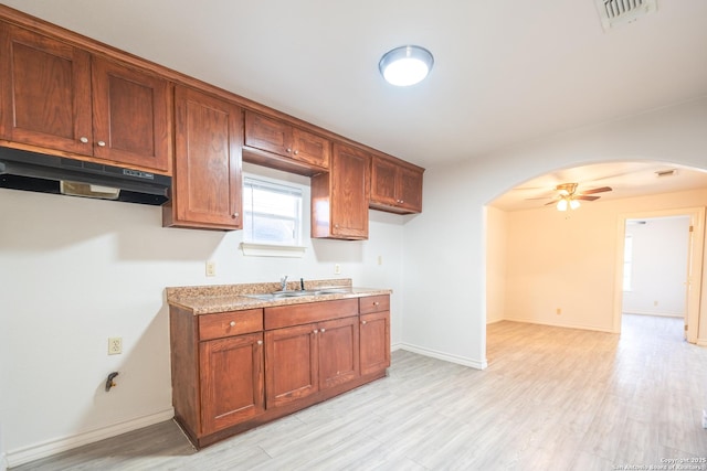 kitchen with arched walkways, visible vents, light wood-style flooring, a sink, and under cabinet range hood