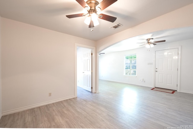 unfurnished room with arched walkways, visible vents, light wood-style flooring, and baseboards