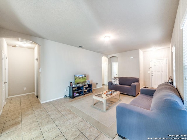 living area with arched walkways, light tile patterned flooring, visible vents, and baseboards