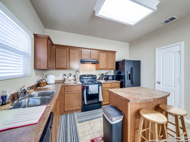 kitchen featuring a center island, visible vents, light countertops, under cabinet range hood, and black appliances