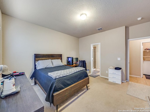 bedroom featuring a textured ceiling, light carpet, connected bathroom, and visible vents