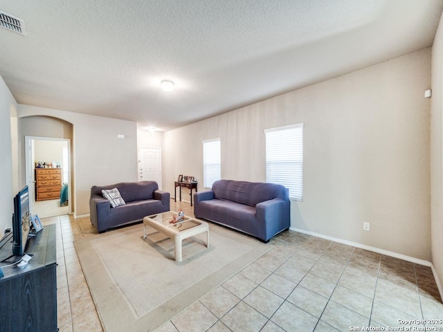 living room featuring visible vents, arched walkways, a textured ceiling, and light tile patterned flooring