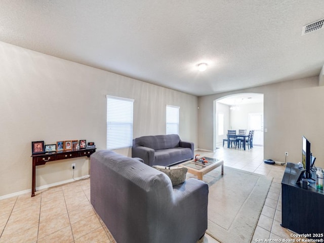 living area featuring arched walkways, visible vents, light tile patterned flooring, a textured ceiling, and baseboards