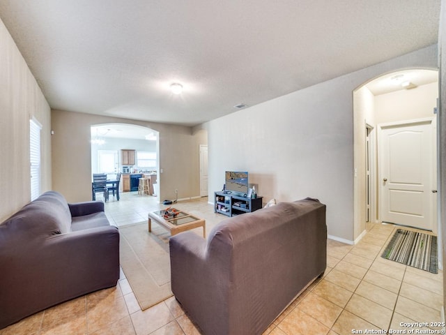 living area featuring arched walkways, light tile patterned flooring, and baseboards