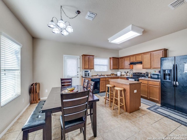 kitchen with a kitchen island, visible vents, light countertops, black appliances, and a kitchen bar