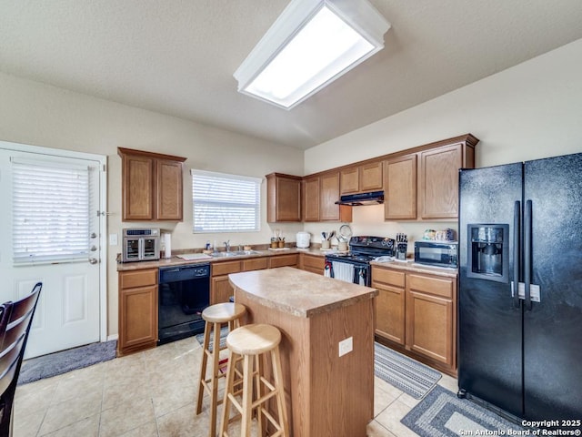 kitchen featuring a breakfast bar area, under cabinet range hood, a sink, a center island, and black appliances