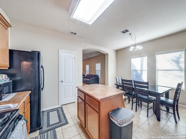 kitchen featuring arched walkways, light countertops, visible vents, hanging light fixtures, and a kitchen island