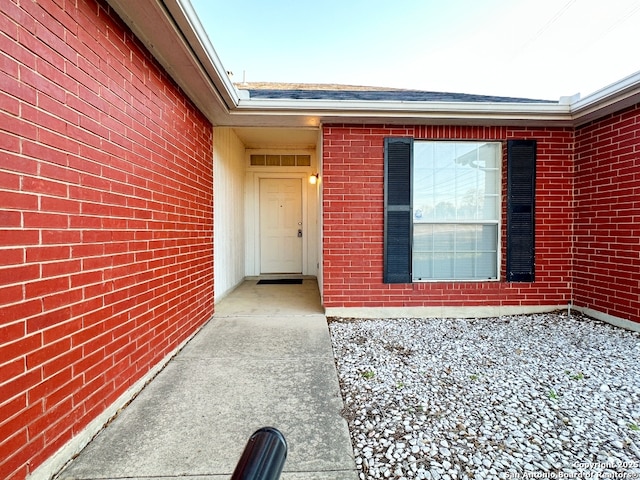 property entrance featuring a shingled roof and brick siding