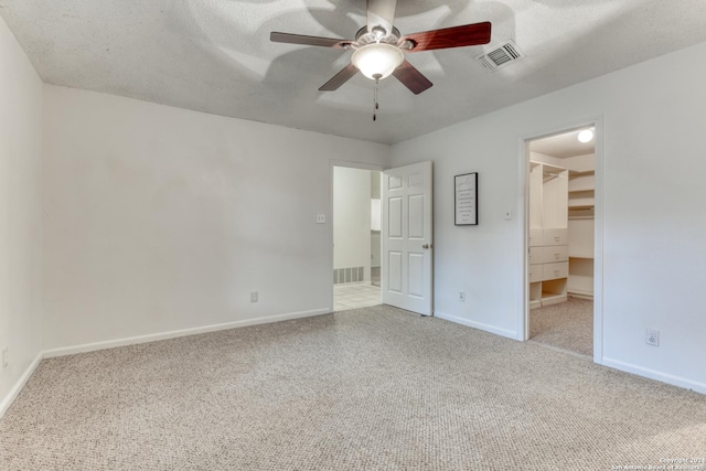 unfurnished bedroom featuring a textured ceiling, visible vents, a walk in closet, and carpet flooring