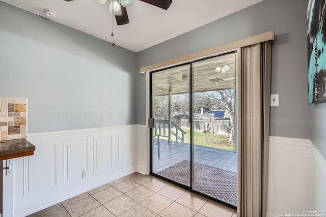 doorway to outside with light tile patterned floors, wainscoting, and a ceiling fan