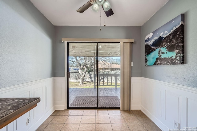 doorway with a wainscoted wall, ceiling fan, and light tile patterned floors