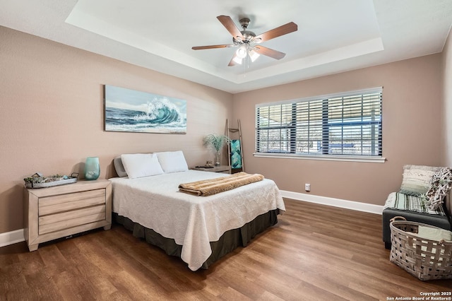 bedroom with a raised ceiling, baseboards, and wood finished floors