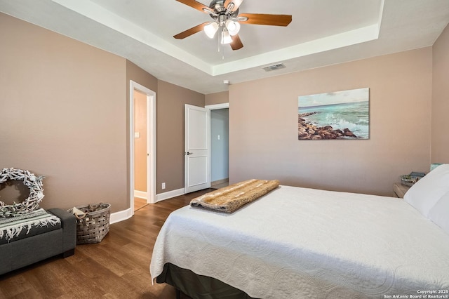 bedroom featuring baseboards, visible vents, a tray ceiling, and wood finished floors