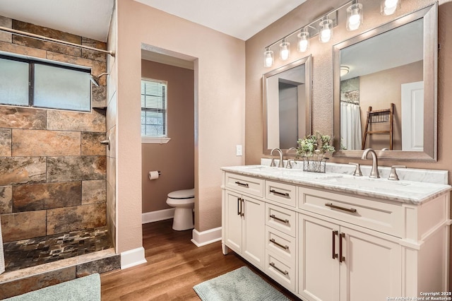 full bath with double vanity, wood finished floors, a sink, and tiled shower