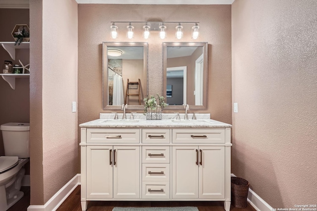 full bath featuring toilet, double vanity, baseboards, and a sink