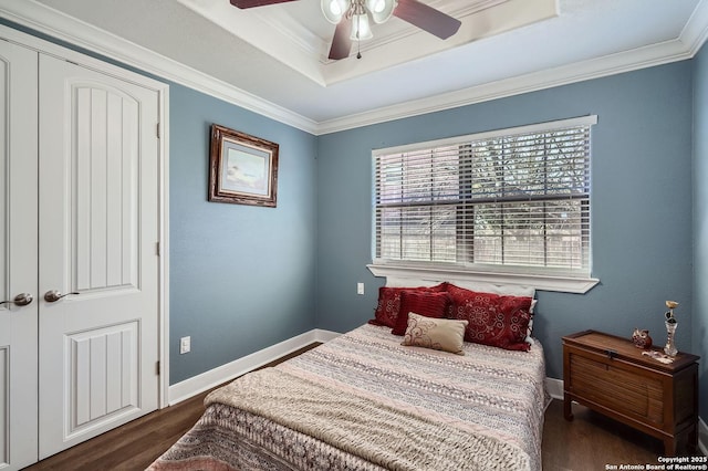 bedroom featuring dark wood finished floors, baseboards, a raised ceiling, and crown molding