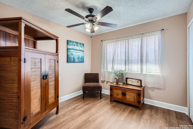 sitting room featuring light wood-type flooring, a ceiling fan, baseboards, and a textured ceiling