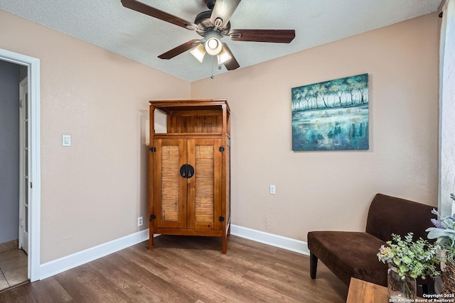 sitting room with ceiling fan, a textured ceiling, baseboards, and wood finished floors