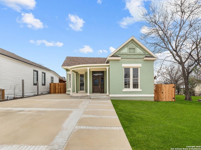 view of front of house featuring roof with shingles, fence, a front yard, a porch, and stucco siding