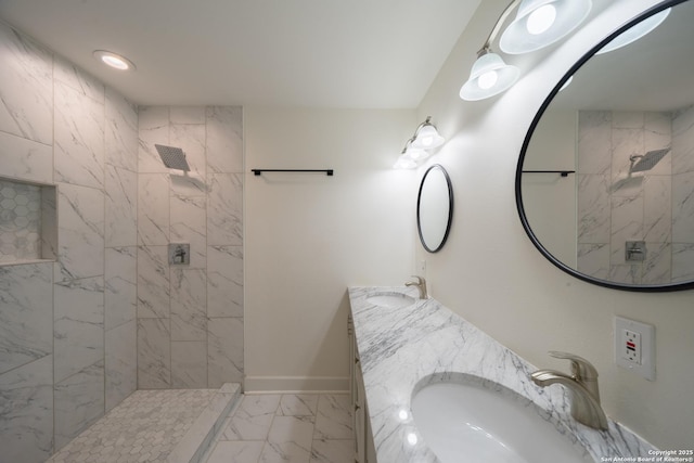 bathroom with marble finish floor, baseboards, a tile shower, and a sink